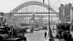 Black and white view of vehicles on quayside with Tyne Bridge beyond